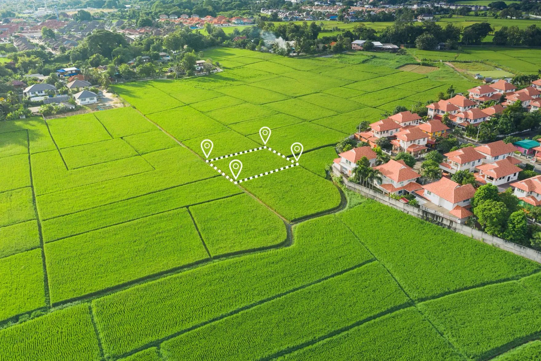 Luftaufnahme grüner Feldflächen am Rand eines Wohngebiets, eine freie Parzelle ist als Baugrundstück eingezeichnet
