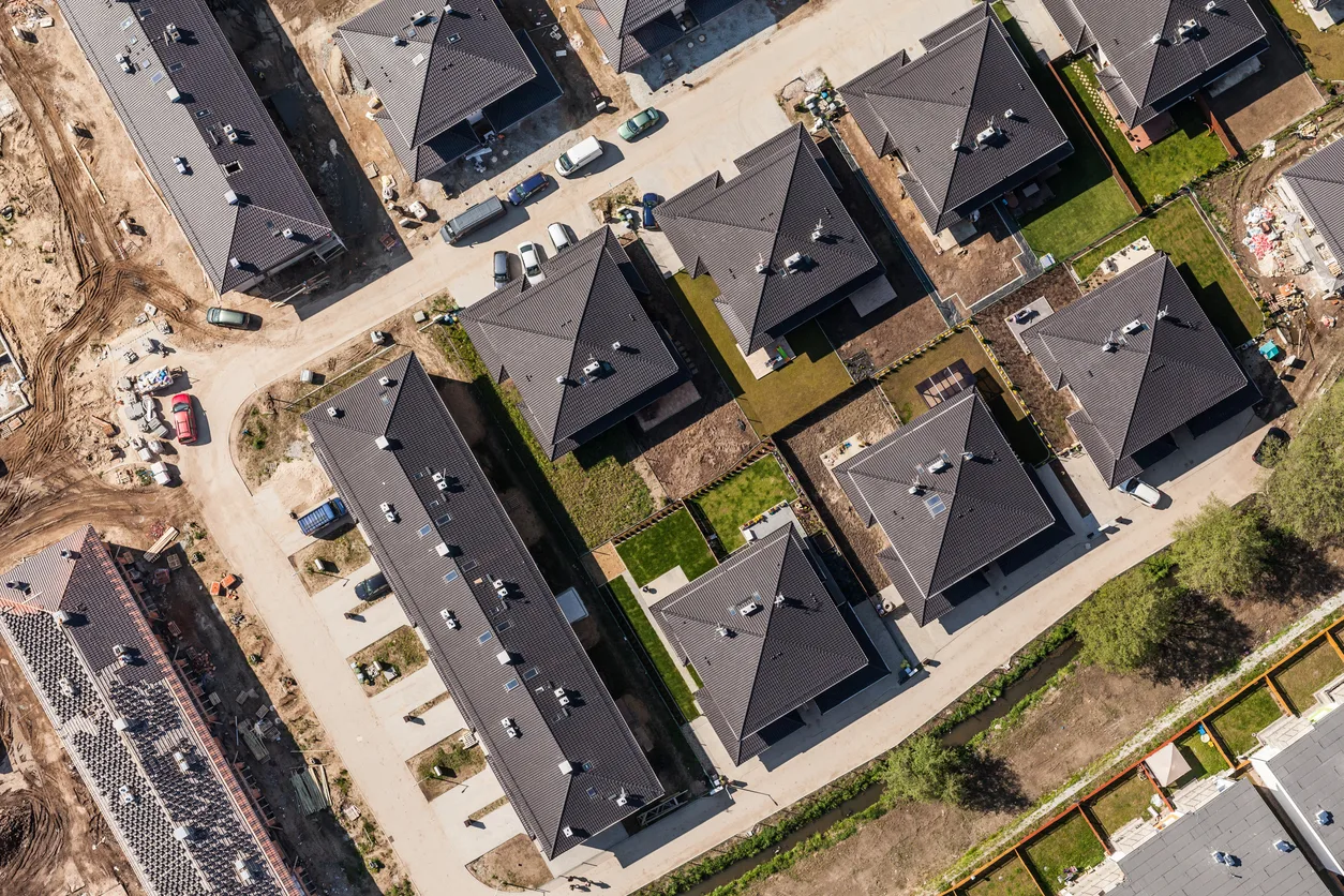 Senkrechte Luftaufnahme eines neuen Wohnquartiers mit dunklen Satteldächern, Stichstraßen und einer angrenzenden Baustelle