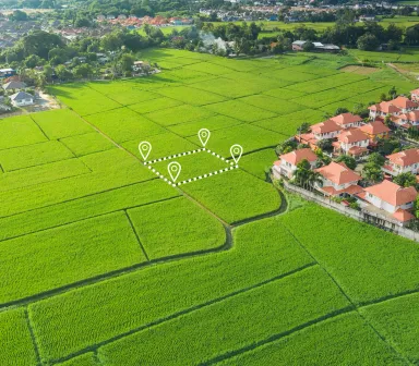 Luftaufnahme grüner Feldflächen am Rand eines Wohngebiets, eine freie Parzelle ist als Baugrundstück eingezeichnet