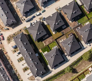 Senkrechte Luftaufnahme eines neuen Wohnquartiers mit dunklen Satteldächern, Stichstraßen und einer angrenzenden Baustelle